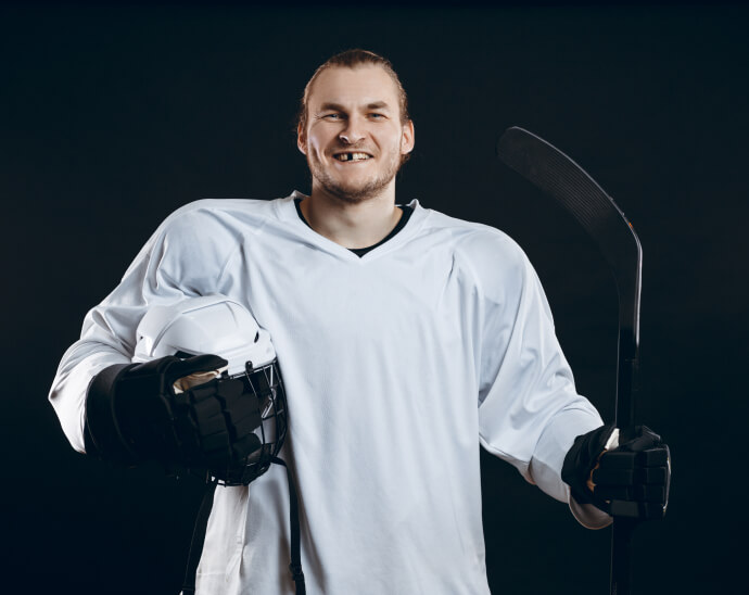 Guy in his hockey uniform smiling with a missing tooth.
