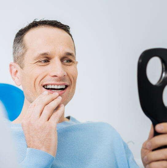 A man looking at his new smile in a handheld mirror.